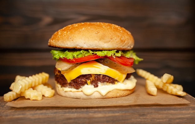 Sabrosa hamburguesa casera con carne de res, lechuga, queso, pepino y papas fritas sobre un fondo de madera