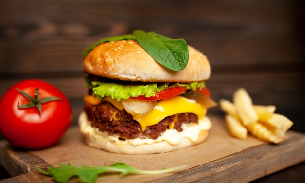 Sabrosa hamburguesa casera con carne de res, lechuga, queso, pepino y papas fritas sobre un fondo de madera