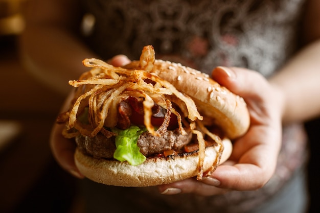 Sabrosa hamburguesa con cebolla en manos femeninas