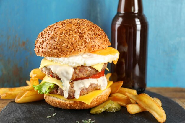 Sabrosa hamburguesa doble con huevo frito en la mesa contra la pared azul