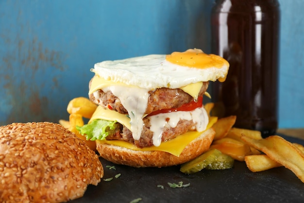 Sabrosa hamburguesa doble con huevo frito en la mesa contra la pared azul