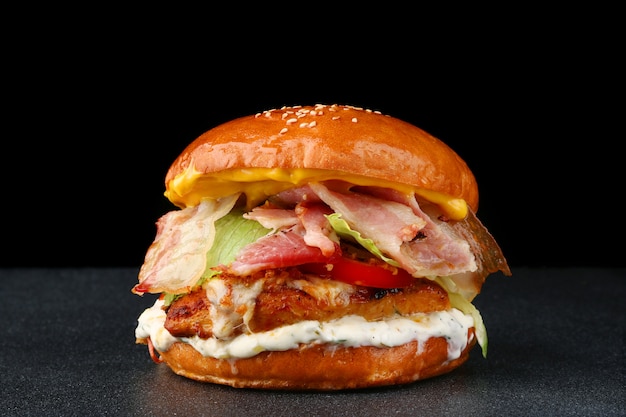 Sabrosa hamburguesa con pollo y tocino sobre fondo oscuro aislado. Hamburguesa casera con verduras frescas y salsa