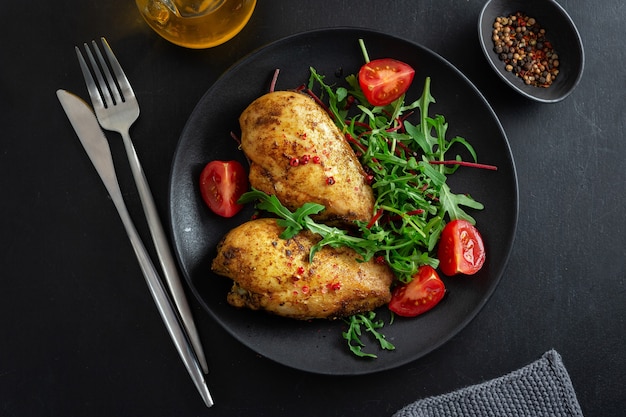 Sabrosa pechuga de pollo a la plancha con verduras y ensalada servida en mesa oscura.