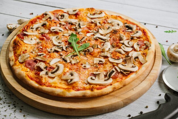 Sabrosa pizza Caprizzioza con salsa de tomate, jamón y champiñones en el fondo de madera blanca