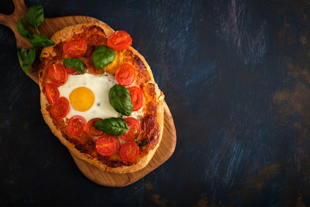 Sabrosa pizza casera con huevo, queso, tomate y albahaca.