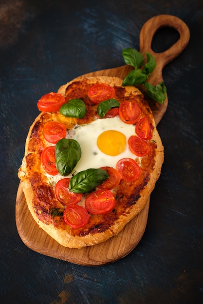 Sabrosa pizza casera con huevo, queso, tomate y albahaca.