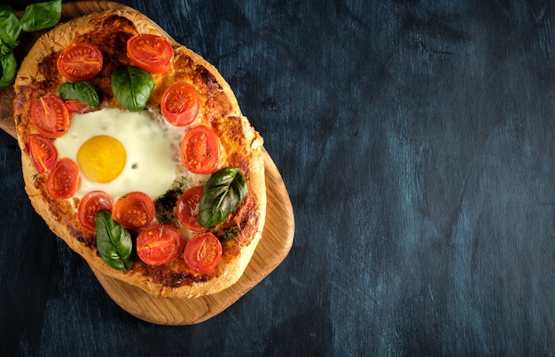 Sabrosa pizza casera con huevo, queso, tomate y albahaca.