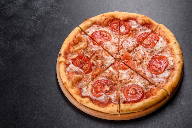 Sabrosa pizza fresca al horno con tomate, queso y albahaca sobre una mesa oscura