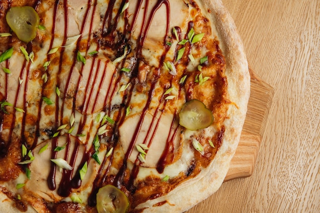 Sabrosa pizza italiana con carne, encurtidos y salsa sobre tabla de madera