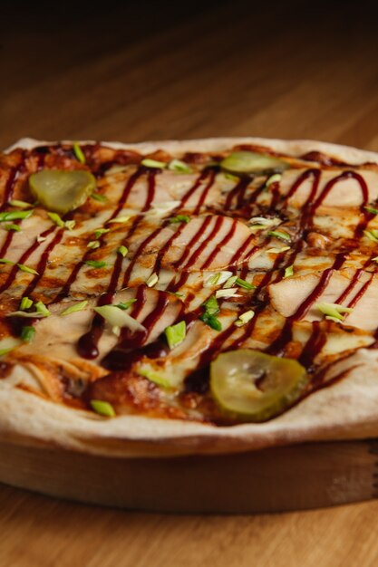 Sabrosa pizza italiana con carne, encurtidos y salsa sobre tabla de madera