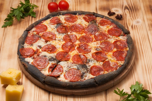 Sabrosa pizza de pepperoni sobre masa negra sobre una tabla de madera