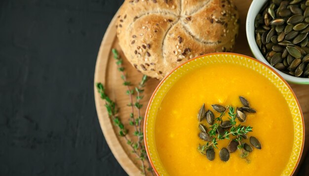 Sabrosa sopa de calabaza casera vegana caliente con semillas, hierbas y pan, sobre un fondo negro