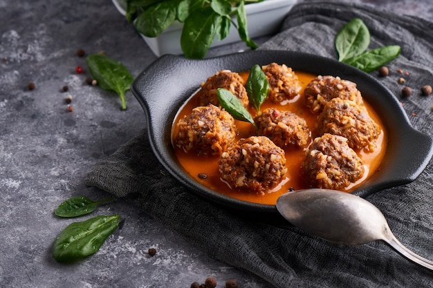 Sabrosas albóndigas caseras con salsa de tomate y espinacas servidas en un plato sobre una mesa de piedra oscura