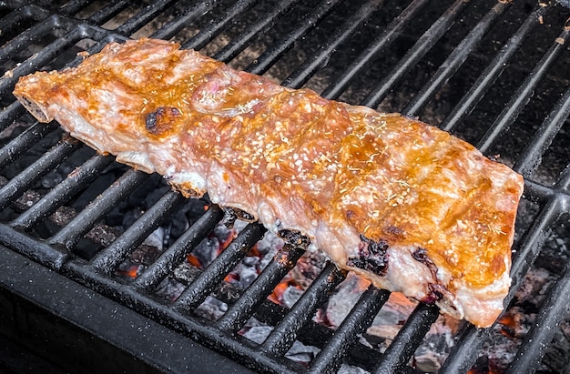 Sabrosas costillas de cerdo en una parrilla de barbacoa. Cerca de delicioso cerdo a la parrilla cocinado en barbacoa de casa jardín en vacaciones. Carne asada crujiente en España.