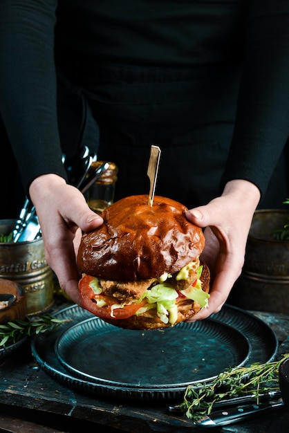 Sabrosas hamburguesas caseras a la parrilla con pollo, tomates y cebollas En las manos Sobre un fondo negro