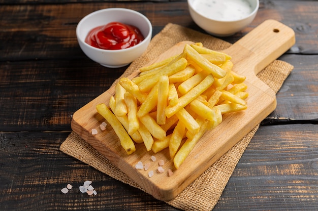 Sabrosas papas fritas en la tabla de cortar, sobre fondo de mesa de madera