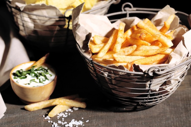Sabrosas patatas fritas en una cesta de metal y patatas fritas en una mesa de madera con luz oscura