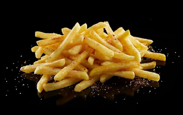 Sabrosas patatas fritas crujientes con sal y pimiento rojo sobre una mesa negra