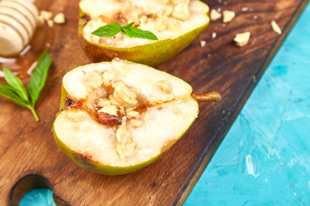 Sabrosas peras asadas con miel y nueces sobre tabla de fondo azul.