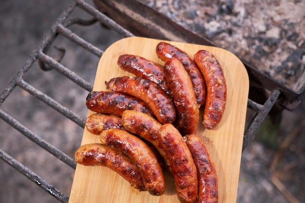 Sabrosas salchichas recién asadas a la parrilla de carbón en tabla de cortar de madera