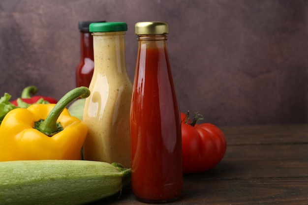 Sabrosas salsas en botellas de vidrio y productos frescos en una mesa de madera de primer plano Espacio para el texto