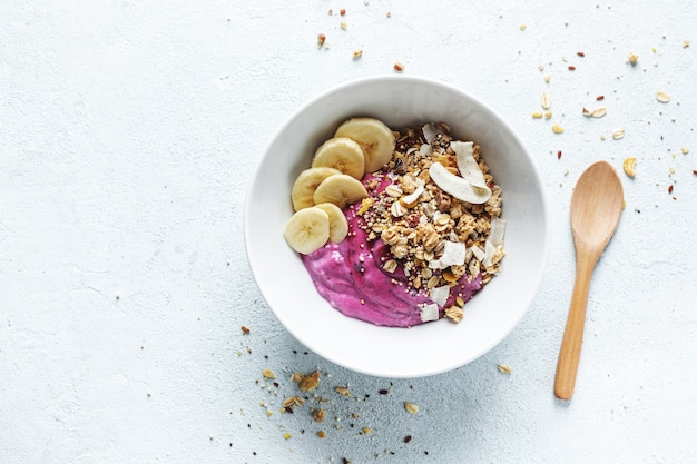 Sabroso y apetitoso desayuno de dieta saludable con granola, yogur de arándanos y plátano servido en un tazón. Vista superior.