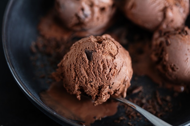 Sabroso y apetitoso helado de chocolate con trozos de chocolate en un plato oscuro sobre fondo oscuro.