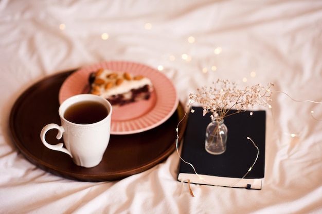 Sabroso café de la mañana en la cama con pastel y cuaderno con flores de cerca. Hora del desayuno.