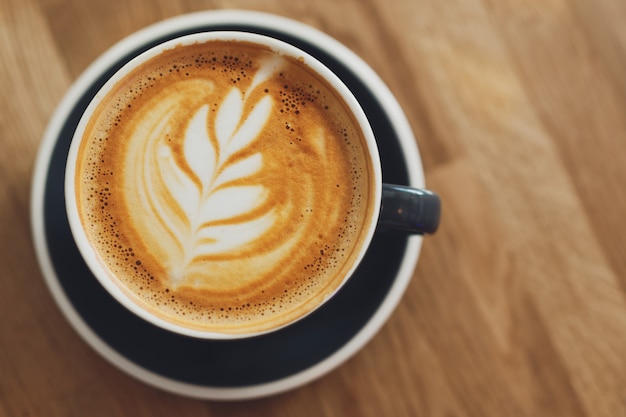 Sabroso capuchino fresco en taza sobre mesa de madera. De cerca