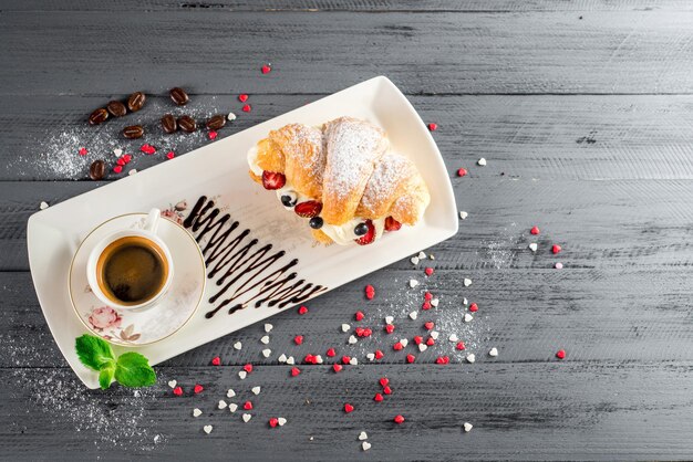 Sabroso croissant con frutas y una taza de café en el fondo de madera