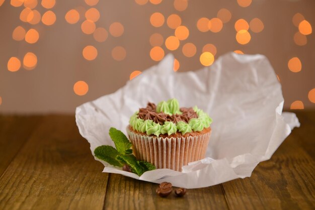 Foto sabroso cupcake con crema de mantequilla sobre una mesa de madera sobre fondo de luces