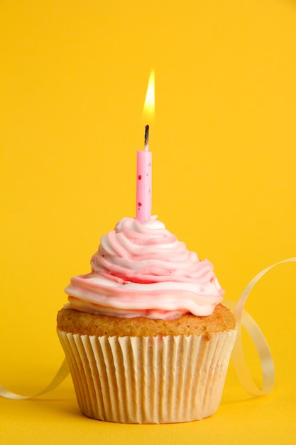 Sabroso cupcake de cumpleaños con vela sobre fondo amarillo