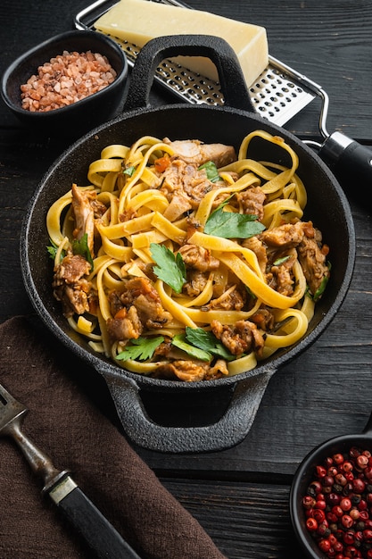 Sabroso estofado de conejo picante con tagliatelle de pasta o pappardelle, en sartén o olla de hierro fundido, sobre mesa de madera negra