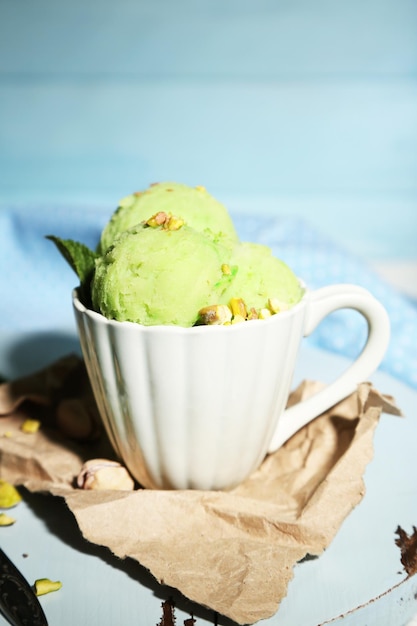 Sabroso helado de pistacho en taza sobre mesa de madera sobre fondo azul.