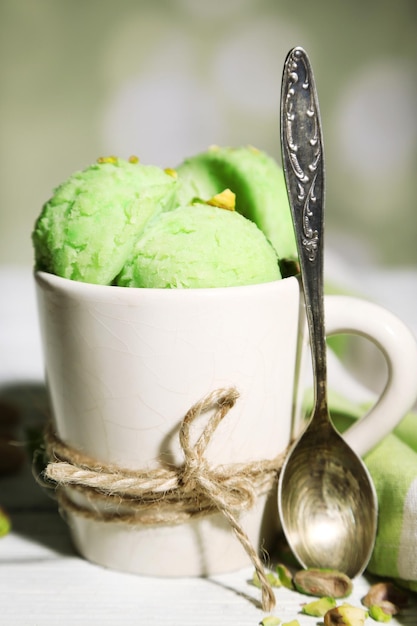 Sabroso helado de pistacho en taza sobre mesa de madera sobre fondo claro