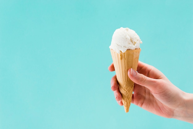 Sabroso helado de vainilla en mano sobre fondo azul