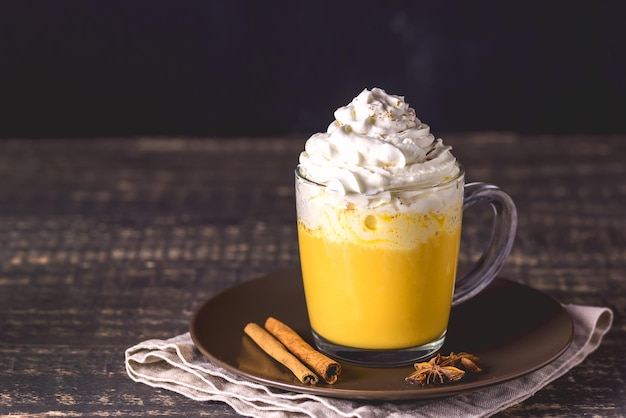 Sabroso Latte de calabaza con crema batida de especias en la parte superior sobre un fondo de madera oscura Bebida caliente de otoño