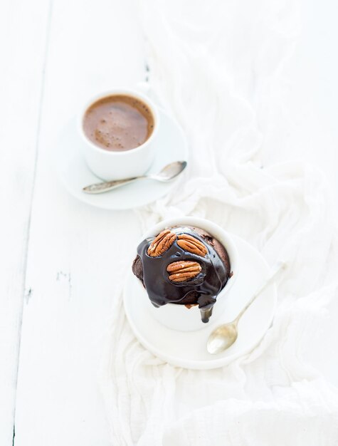 Sabroso panecillo marrón casero con ganache de chocolate glaseado de nueces pecanas y café en una taza de bakind separada