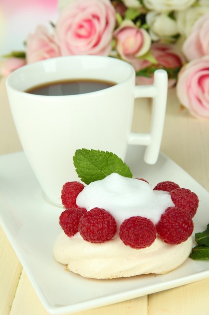 Sabroso pastel de merengues con bayas y una taza de café en una mesa de madera