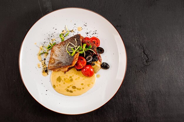 Sabroso pescado dorado a la parrilla con verduras hervidas y salsa sobre fondo de madera