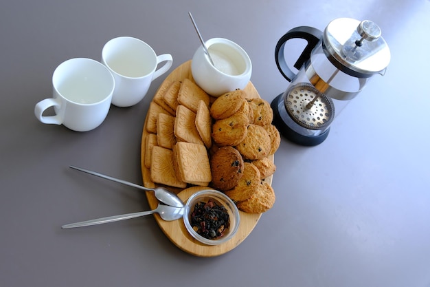 Un sabroso refrigerio, dos tazas de té negro y un plato de galletas de avena, una tabla de madera sobre el fondo gris, té de hojas.