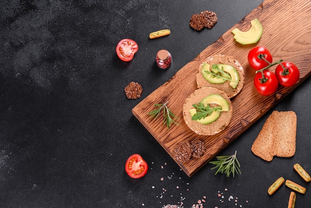 Sabroso sándwich fresco con pasta de hígado, trozos de aguacate y rúcula sobre una mesa de hormigón oscuro