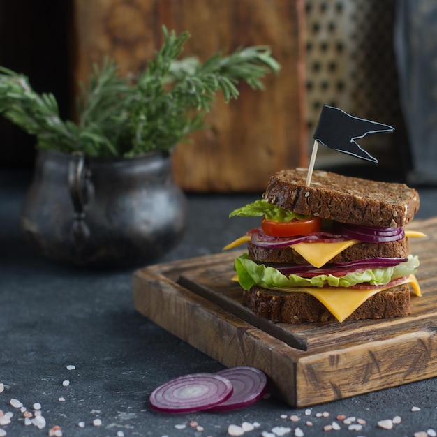 Sabroso sándwich hecho de pan, tomates, salchichas, cebolla y lechuga en una mesa de piedra oscura