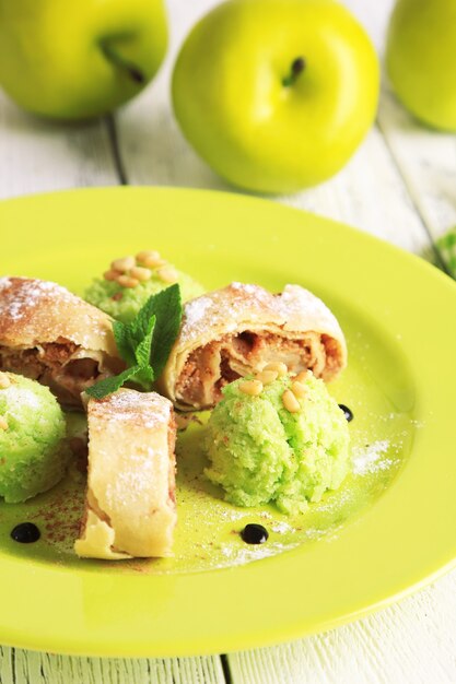 Sabroso strudel de manzana casero con nueces, hojas de menta y helado en la placa, sobre fondo de madera