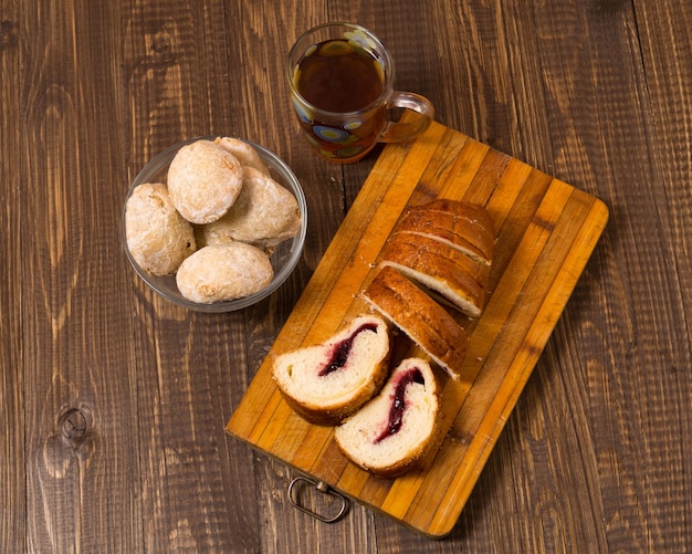 Sabroso té en una taza, bollos en plato y mermelada y pan cortado están en la mesa de madera