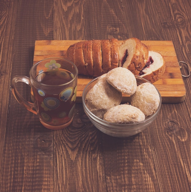 Sabroso té en una taza, bollos en plato y mermelada y pan cortado están sobre la mesa