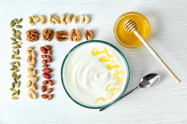 Sabroso yogur con miel en un tazón y diferentes nueces en la mesa