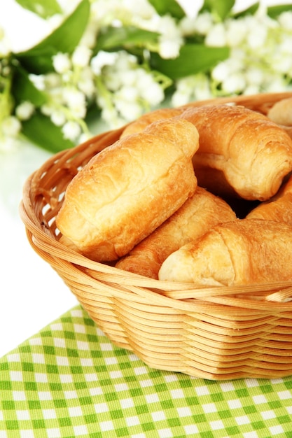 Sabrosos croissants en cesta de mimbre en la mesa sobre fondo blanco.