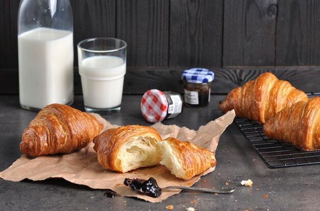 Sabrosos croissants frescos con mermelada y leche en mesa gris