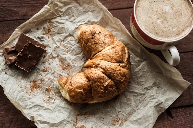 Sabrosos croissants con taza de café y chocolate en mesa de madera